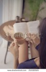 stock-photo-woman-drinking-tea-while-reading-a-book-at-home-rear-view-212320525